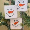Three snowmen tree decorations with friendly faces.