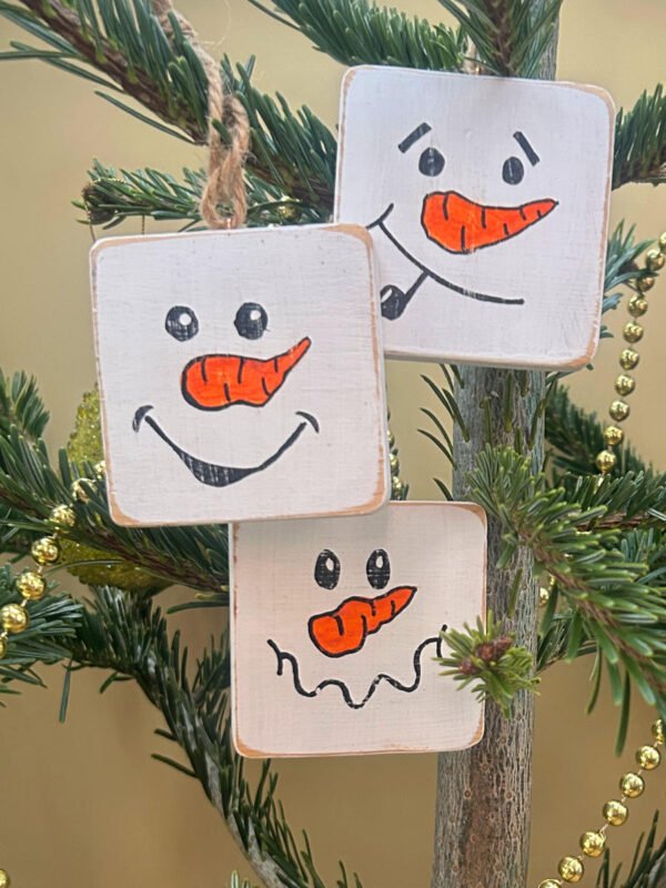 Three snowmen tree decorations with friendly faces.
